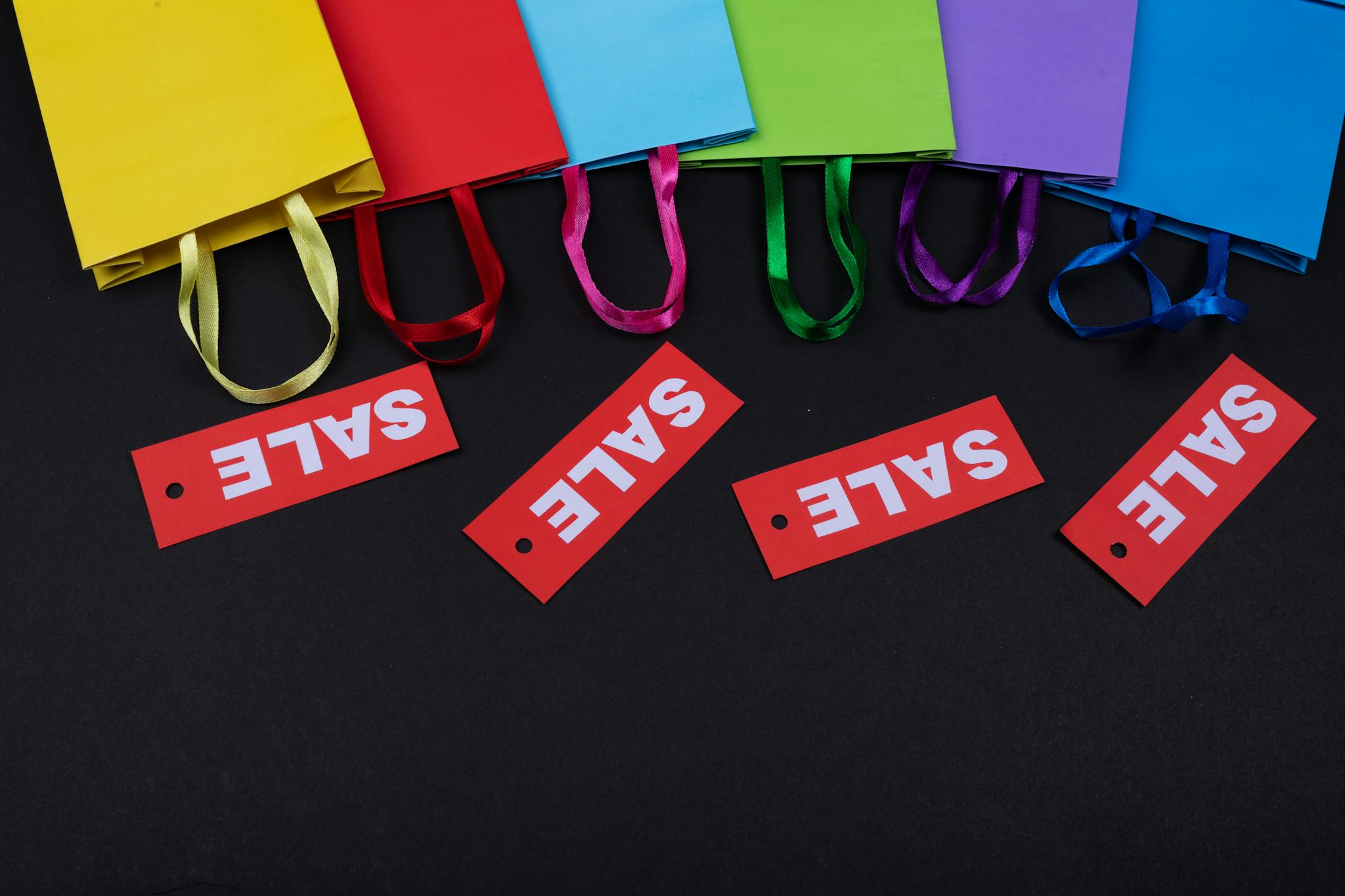 Vibrant shopping bags with bright red sale tags on a dark background, ideal for retail promotions.